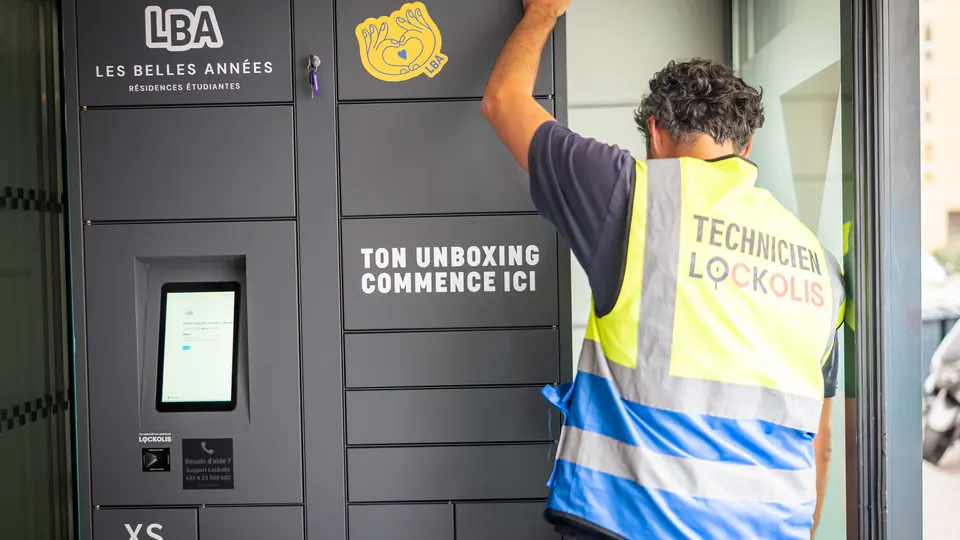 Un technicien Lockolis règle le haut d’une consigne connectée installée dans une entrée vitrée