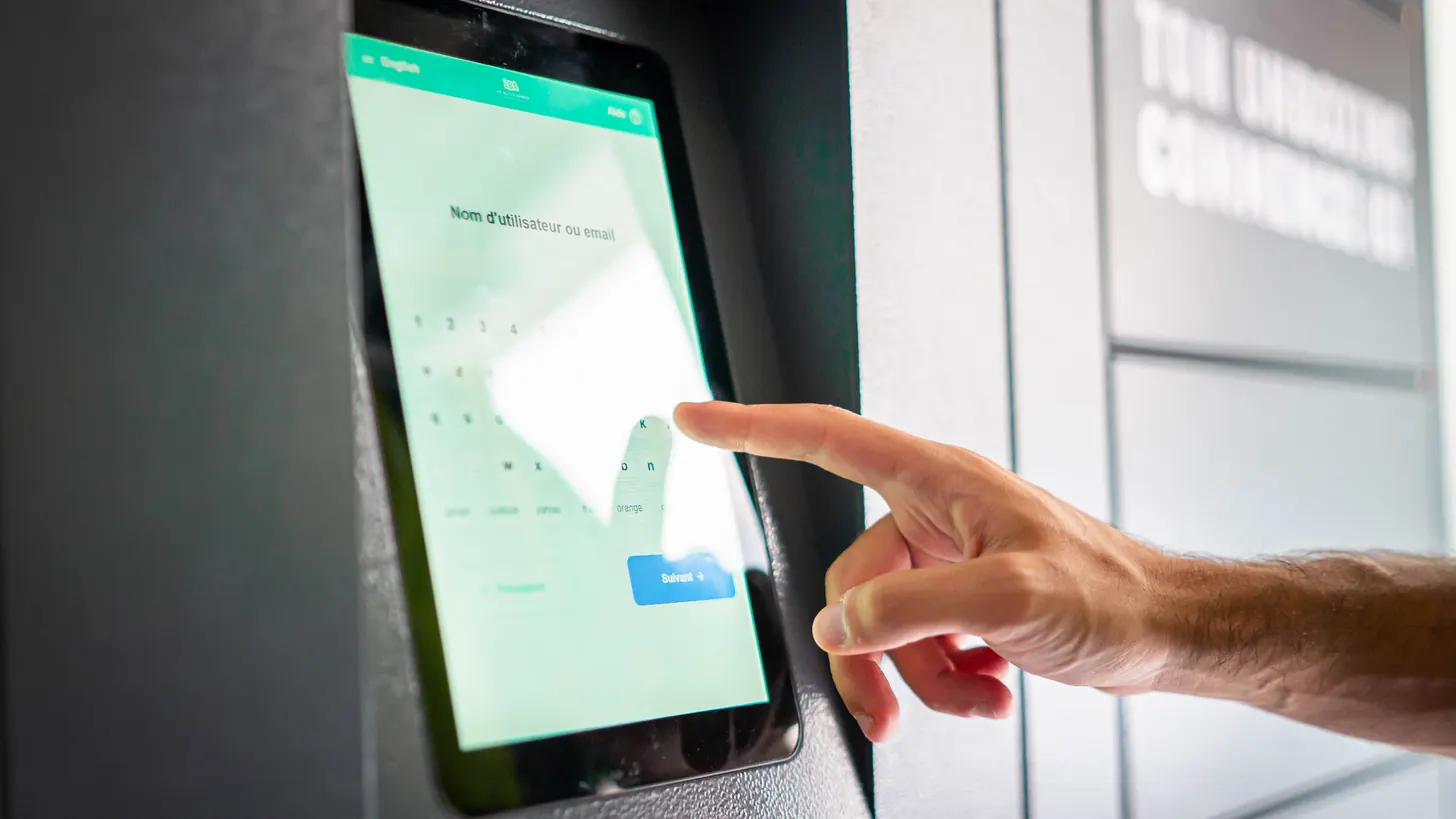Doigt sur l'écran tactile d'un casier connecté, sur la page d'identification de l'utilisateur