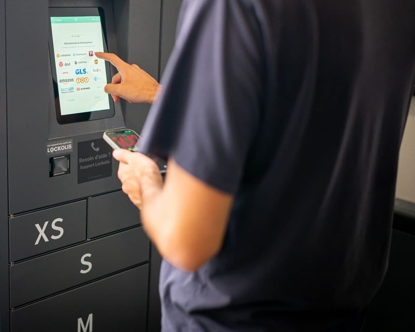 A person, phone in hand, at the locker's touchscreen